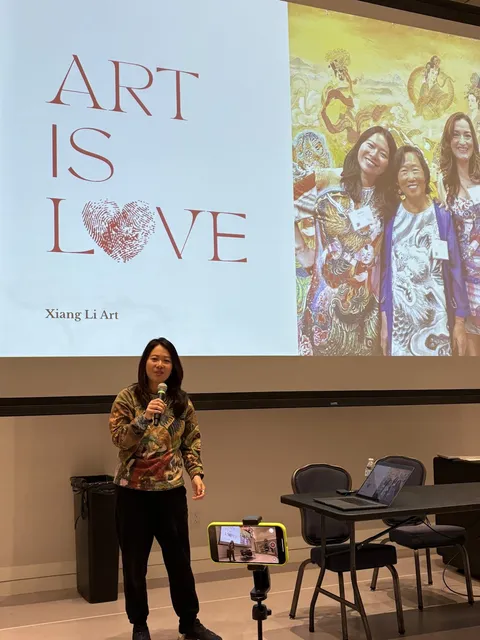 Fei Wu speaking with a microphone in front of a slide reading Art Is Love at the College of the Holy Cross