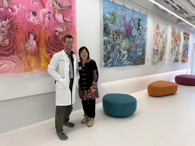 Xiang Li beside a LabCentral scientist in a white lab coat, in front of large silk paintings