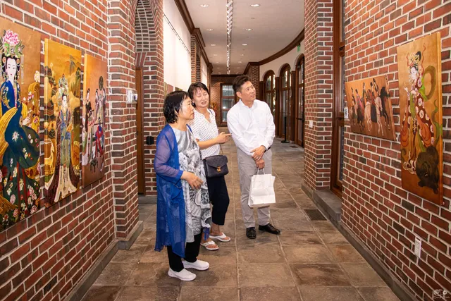 Xiang Li with two guests in a brick gallery corridor hung with empress paintings