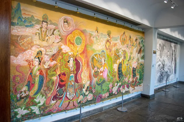 A wall-length silk painting of Chinese empresses in jewel colors hanging in a gallery at the New England Botanic Garden, an ink mural beyond it