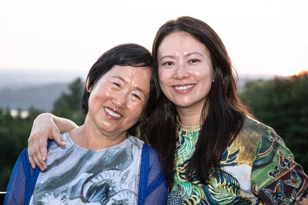 Xiang Li and Fei Wu smiling together on the terrace at Tower Hill, the garden and hills behind them at sunset