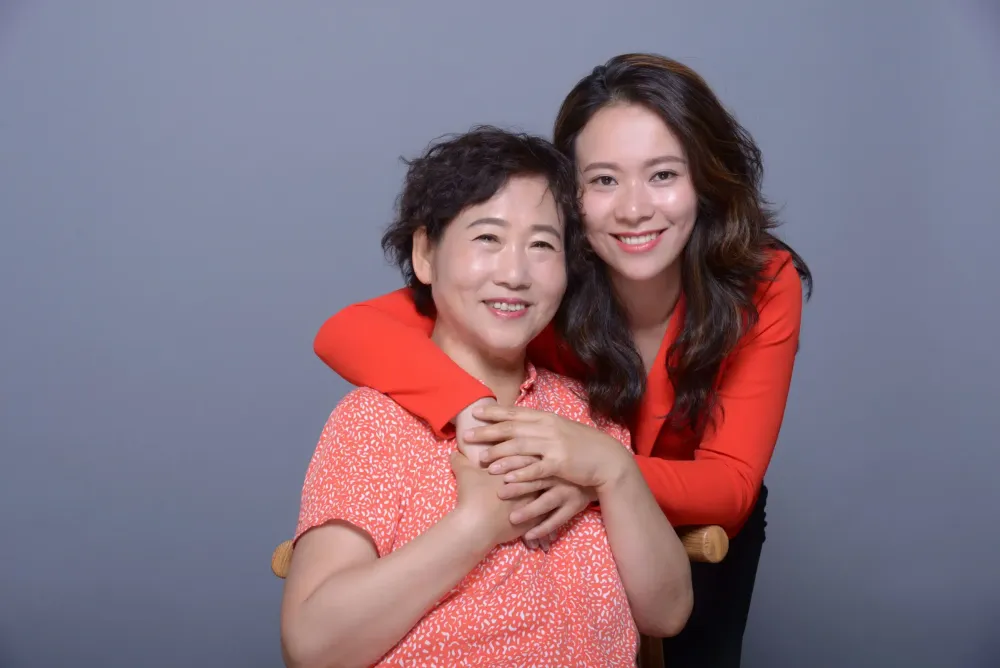 Xiang Li and her daughter Fei Wu in a studio portrait, Fei’s arms around her mother’s shoulders