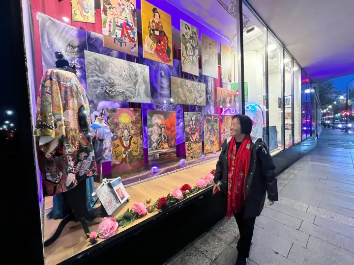 Xiang Li standing outside a lit window display of her empress paintings at the Denholm Building at night