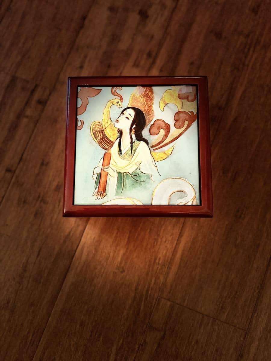Top view of a red lacquer jewelry box with a painted tile showing an empress in white and green robes beneath a golden phoenix.