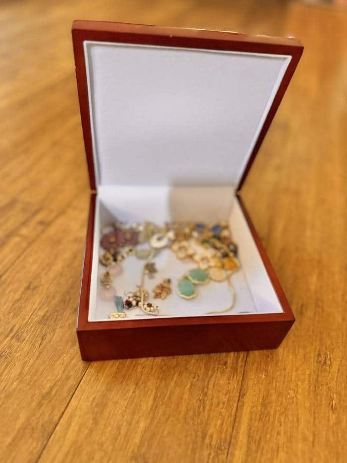 The jewelry box open, its white-lined interior holding earrings, chains and stone pendants.