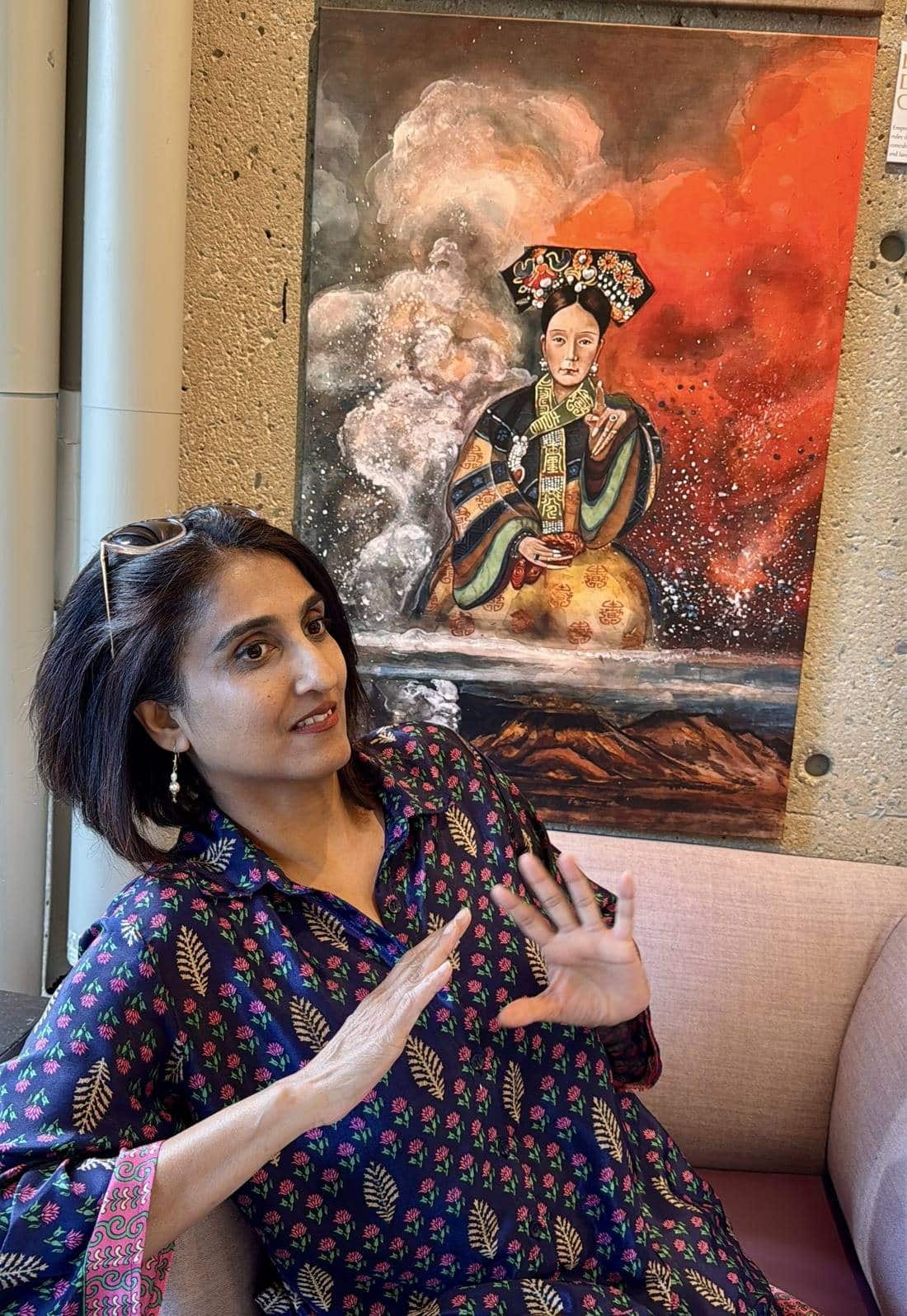 Tripti seated in front of Xiang Li's painting of Empress Dowager Cixi, who is shown enthroned between billowing grey smoke and a field of red.