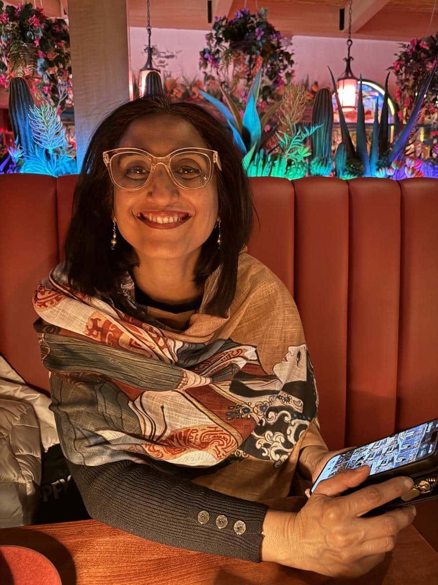 Tripti wearing the same scarf draped over one shoulder in a restaurant booth, smiling at the camera.