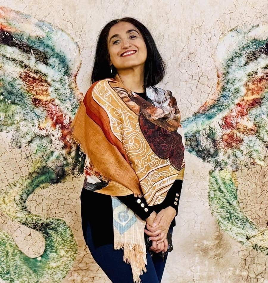 Tripti wearing the ochre and oxblood Empress Liang Na scarf, standing in front of a painted mural of wings.
