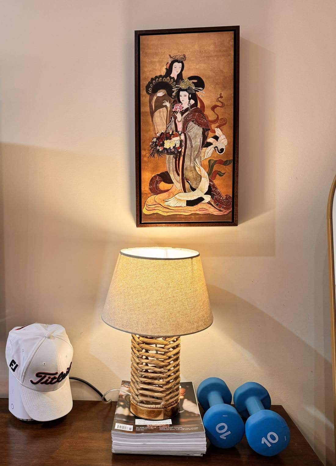 Framed vertical canvas print of two Chinese empresses with cranes and a peacock-feather fan, hanging on a wall above a lit lamp.
