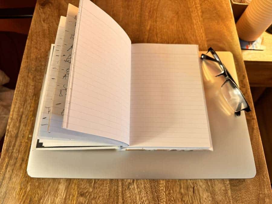 The same journal open to a fresh ruled page, with earlier handwritten notes visible on the pages behind.